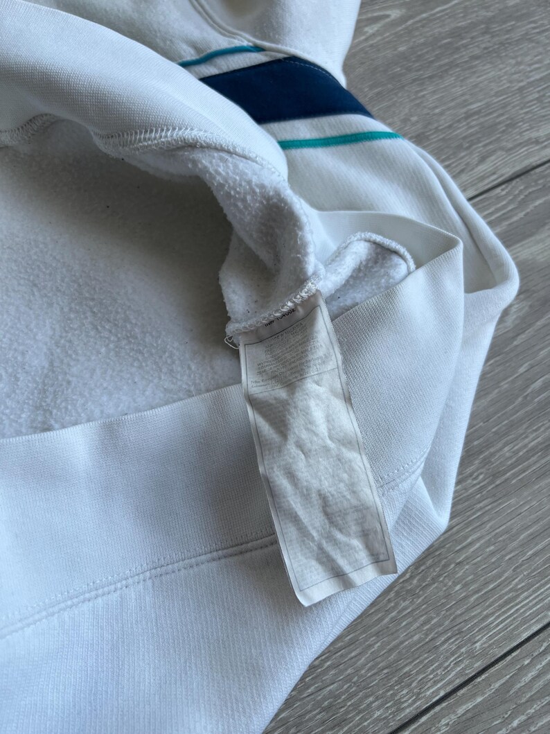 Puede incluir: Sudadera con capucha blanca con un dise&ntilde;o de rayas azules y turquesas en la parte superior del pecho. El interior es de un material suave y afelpado. Una etiqueta est&aacute; adherida al dobladillo inferior.