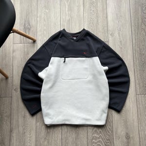May include: A black and white fleece pullover with a V-neck and a small red Nike logo on the chest. The pullover has a pocket on the front and a zipper. The sleeves are long.
