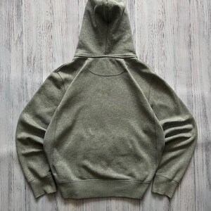 Puede incluir: Una sudadera con capucha gris jaspeado con capucha con cord&oacute;n. La vista trasera de la sudadera muestra la capucha y los hombros. La sudadera con capucha tiene un dobladillo y pu&ntilde;os acanalados. La tela parece ser un material suave y de peso medio.