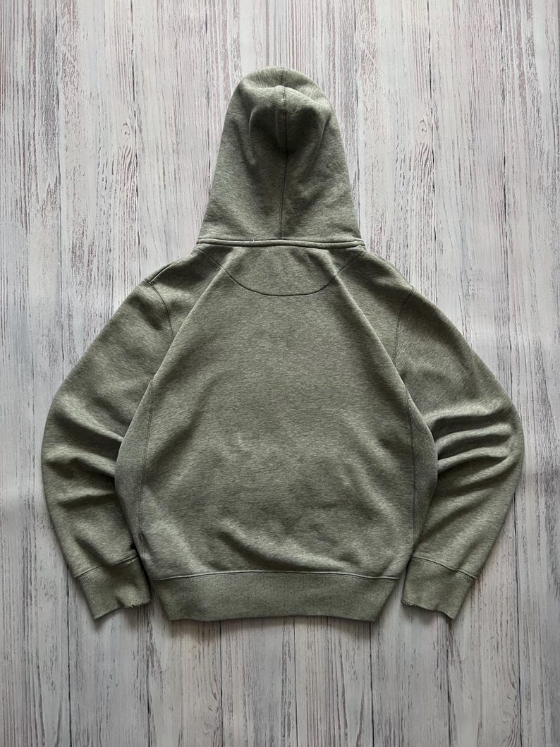 Puede incluir: Una sudadera con capucha gris jaspeado con capucha con cord&oacute;n. La vista trasera de la sudadera muestra la capucha y los hombros. La sudadera con capucha tiene un dobladillo y pu&ntilde;os acanalados. La tela parece ser un material suave y de peso medio.