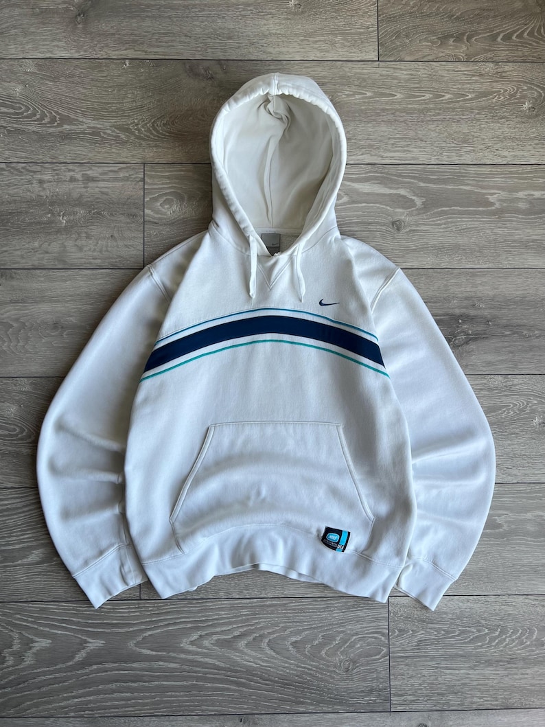 Puede incluir: Sudadera con capucha blanca con bolsillo delantero y dise&ntilde;o de rayas horizontales en azul marino y verde azulado. Presenta el logotipo de Nike swoosh en el pecho y un peque&ntilde;o parche en la parte inferior izquierda.