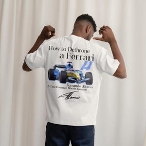 May include: White t-shirt featuring a Formula 1 race car graphic with the text "How to Dethrone a Ferrari" and "Fernando Alonso, 2-Time Formula 1 World Champion." The design includes the number 14 and a signature.