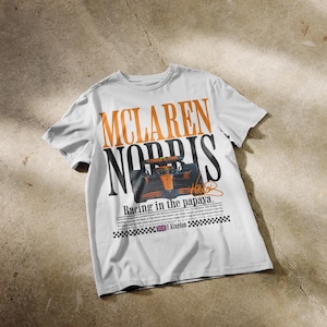 May include: White t-shirt featuring the words "McLaren Norris" in orange and black, with a graphic of a race car. The text "Racing in the papaya" is below the car image, along with additional text and a signature.