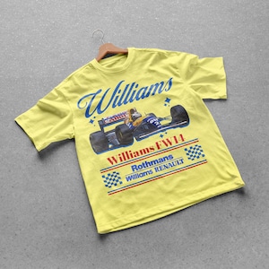 May include: A yellow t-shirt featuring a vintage Williams FW14 race car design. The shirt has the word "Williams" in blue script across the top, with the car graphic below. The text "Rothmans Williams Renault" is also visible.