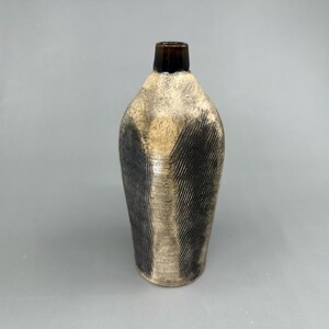Könnte beinhalten: Eine Keramikvase mit einer dunkelbraunen Glasur an der Oberseite und einer hellbraunen und schwarzen Glasur am Körper. Die Vase hat eine strukturierte Oberfläche mit einem Linienmuster.