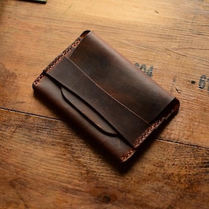 May include: A brown leather wallet with a fold-over flap and stitching detail.
