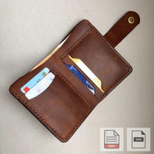 以下が含まれることがあります： 複数のカードスロットと紙幣入れが付いた、開いた茶色の革製財布。財布はスナップ留めで固定されています。いくつかのクレジットカードがスロットに見えます。財布は手作りで、ステッチが見えます。