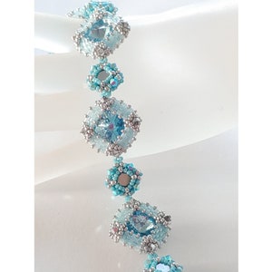 Könnte beinhalten: Ein zartes Armband aus blauen und silbernen Perlen. Das Armband zeigt ein sich wiederholendes Muster aus kleinen Blüten und größeren, facettierten Perlen. Das Armband wird mit einem silbernen Verschluss befestigt.