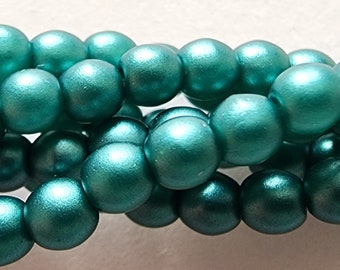 May include: Strands of teal-colored, round wooden beads. The beads have a metallic sheen, and are strung together. The beads are approximately 10mm in diameter. The beads are likely for jewelry making or craft projects.