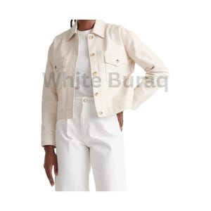 May include: Cream-colored jacket with a collared neckline, two chest pockets, and gold-colored buttons. The jacket is paired with a white t-shirt and white pants. The jacket has a classic, tailored design.