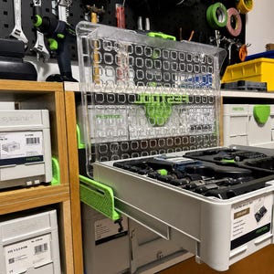 Puede incluir: Un organizador de herramientas de plástico transparente y verde con un cajón extraído, que revela varias herramientas. El organizador forma parte de un sistema de almacenamiento más grande, con contenedores de almacenamiento blancos y grises adicionales visibles. Las herramientas cuelgan de una panel perforado negro.