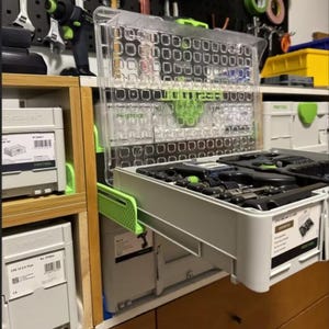 May include: A clear plastic and gray tool organizer with a pull-out drawer, filled with various tools. The organizer is part of a larger system of gray storage containers. The background shows tools hanging on a pegboard.