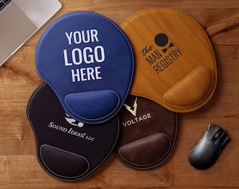 May include: A collection of ergonomic mouse pads in various colors, including blue, brown, and black, with integrated wrist rests. Each pad features a unique logo or text, such as "YOUR LOGO HERE" and "the MAN REGISTRY". A wireless mouse is also present.
