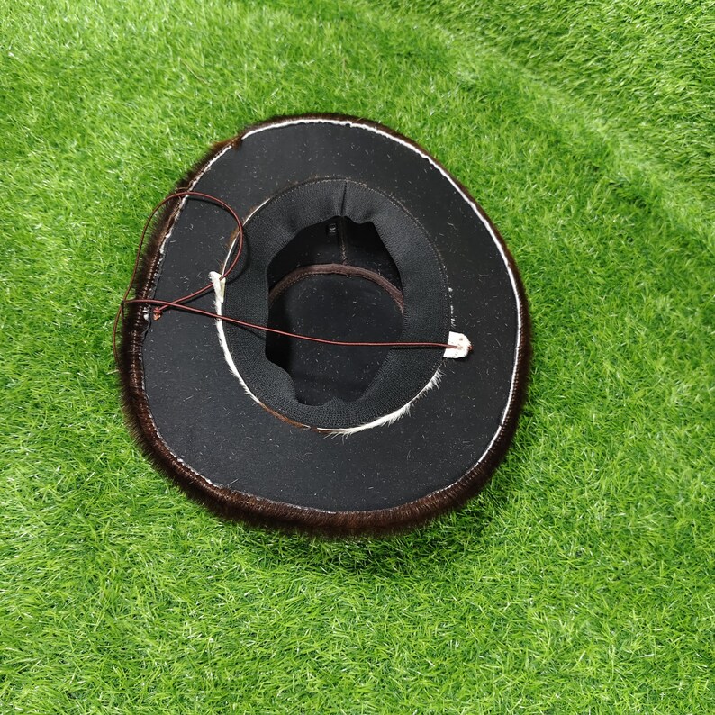 Pode incluir: Um chap&eacute;u preto com acabamento em pele castanha e uma correia de queixo em couro castanho. O interior do chap&eacute;u &eacute; preto com uma faixa castanha. O chap&eacute;u est&aacute; sobre uma superf&iacute;cie verde.