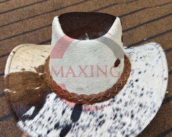 May include: Cowboy hat with a spotted cowhide pattern in white, brown, and black. The hat has a brown leather braided band around the crown and a dark brown top.