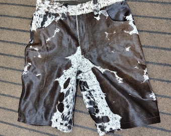 May include: Cowhide shorts in a brown and white spotted pattern. The shorts have a classic five-pocket design with a button and zipper closure. The shorts are made of a soft, textured material.