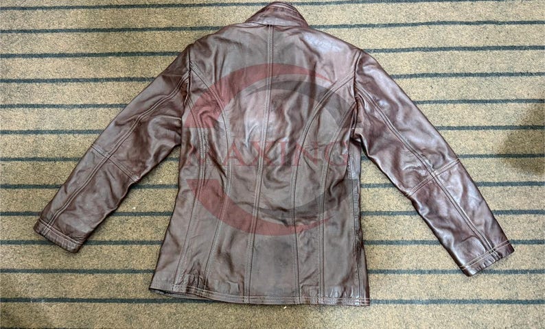 May include: A brown leather jacket with a collared neckline and long sleeves. The jacket has a tailored fit and visible stitching details. The back of the jacket is visible, showing vertical seams and a classic design.