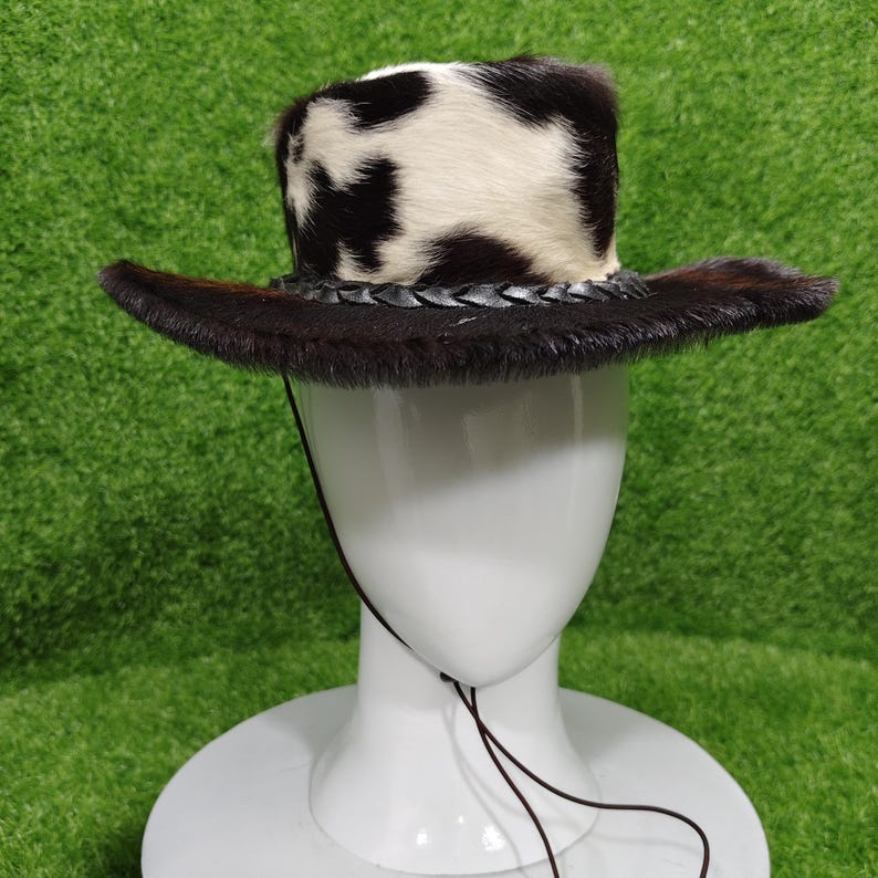 Pode incluir: Chap&eacute;u de cowboy com coroa manchada em preto e branco e aba marrom escuro. O chap&eacute;u apresenta uma faixa de couro tran&ccedil;ado e uma tira de queixo. O chap&eacute;u &eacute; exibido em uma cabe&ccedil;a de manequim branca sobre um fundo verde.