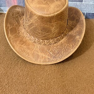 May include: A brown cowboy hat with a snakeskin pattern. The hat has a braided band around the crown and a wide brim. The hat is made of leather and has a vintage appearance.