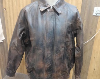 Può includere: Una giacca in pelle marrone scuro con finitura vissuta, dotata di colletto classico, maniche lunghe, chiusura frontale con zip nascosta da una patta con bottoni a pressione e orlo a coste. Presenta dettagli con cuciture verticali.