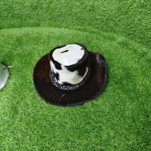 Pode incluir: Um chap&eacute;u de cowboy com aba castanha escura e coroa com padr&atilde;o branco e preto. O chap&eacute;u apresenta uma faixa de couro tran&ccedil;ado ao redor da base da coroa. O chap&eacute;u &eacute; feito de pele.
