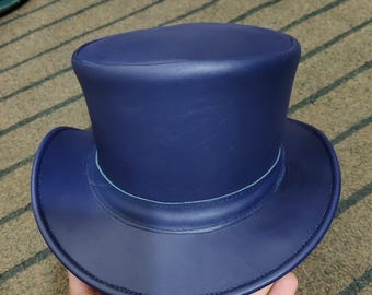 May include: A navy blue top hat with a rounded crown and a wide brim. The hat has a light blue band around the base of the crown. The hat is made of a smooth material.