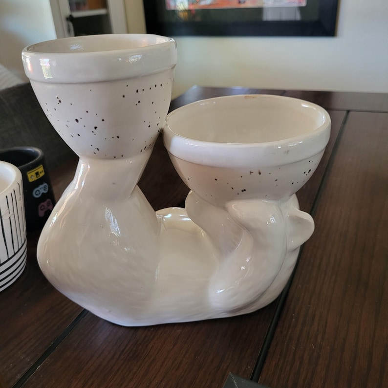 May include: White ceramic planter shaped like a cat holding two smaller white ceramic pots. The pots have a speckled brown glaze.