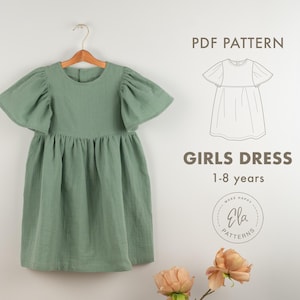 May include: Sage green girls dress with flutter sleeves hanging on a wooden hanger. The dress has a gathered waist and a round neckline. Text on the image reads "GIRLS DRESS 1-8 years" and "PDF PATTERN".