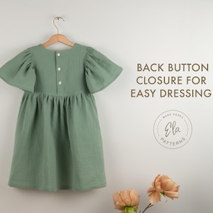May include: A sage green dress with flutter sleeves hangs on a wooden hanger. The dress features a back button closure and a gathered skirt. Text on the right reads "BACK BUTTON CLOSURE FOR EASY DRESSING!" with a circular logo below.