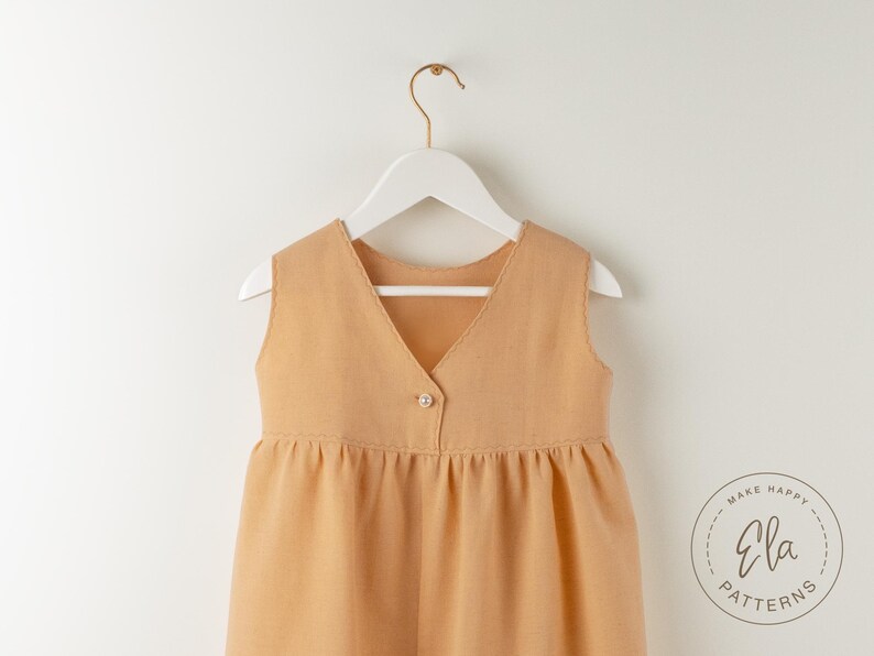 May include: A sleeveless, light brown dress with a V-neck and a single button closure. The dress is hanging on a white hanger against a white background. The dress has a gathered waist and a flared skirt. The logo "Ela Patterns" is visible.