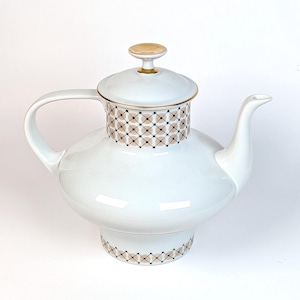 May include: White ceramic teapot with a gold-trimmed lid and handle. The upper section features a geometric pattern in tan and black. The lid has a gold knob. The teapot has a bulbous body and a spout.