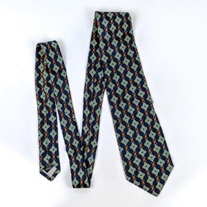 May include: A navy blue tie with a repeating pattern of gold chain links, brown ovals, and green diamond shapes. The tie is made of a smooth fabric and is displayed on a white background. The tie is a classic accessory for formal or business attire.