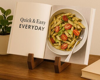 May include: An open cookbook titled "Quick & Easy EVERYDAY" displays a pasta dish with tomatoes and basil. The book rests on a wooden stand. A small potted plant is visible in the background.