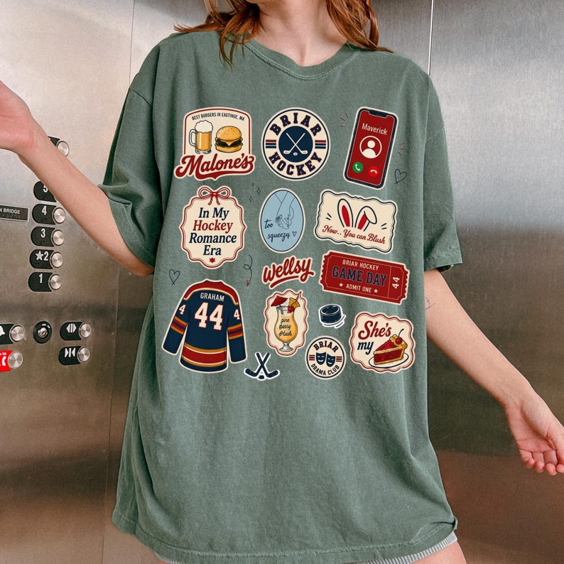 Op de afbeelding: Saliegroen t-shirt met diverse grafische patches. Patches zijn onder meer een hockeytrui, een telefoon, een stuk taart en tekst met de tekst "Briar Hockey", "In My Hockey Romance Era" en "Game Day".