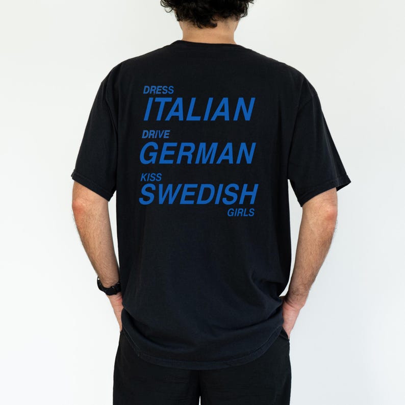 以下が含まれることがあります： 背中に青い文字が入った黒いTシャツ。「DRESS ITALIAN DRIVE GERMAN KISS SWEDISH GIRLS」と書かれています。このシャツはクルーネックです。