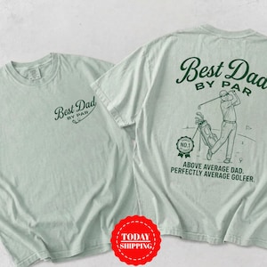 May include: A light sage green t-shirt featuring dark green graphics. The front displays the text Best Dad By Par. The back shows a golfer with a golf bag, a No. 1 badge, and the text Best Dad By Par, Above Average Dad, Perfectly Average Golfer.
