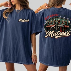 May include: Navy blue t-shirt with the word "Malone's" in a cursive font on the front. The back of the shirt features a graphic of a restaurant with the text "Best Burgers in Hastings, NE!" and "Malone's".