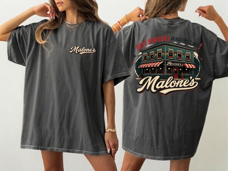 May include: Dark grey t-shirt with the Malone's logo on the front and a restaurant graphic on the back, with the text "Best Burgers in Hastings, MA!". The shirt has a vintage, worn appearance.