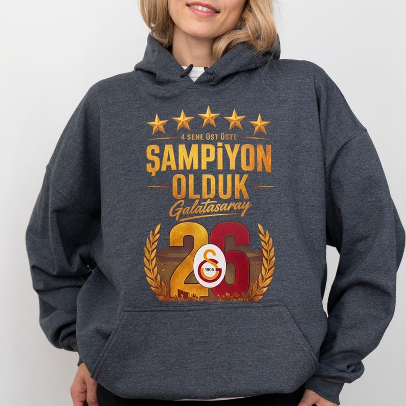 Puede incluir: Sudadera con capucha gris oscuro con un gr&aacute;fico dorado y rojo. El gr&aacute;fico incluye texto y el n&uacute;mero 26, con el logotipo del Galatasaray. El texto dice "4 SENE &Uuml;ST &Uuml;STE ŞAMPİYON OLDUK Galatasaray".