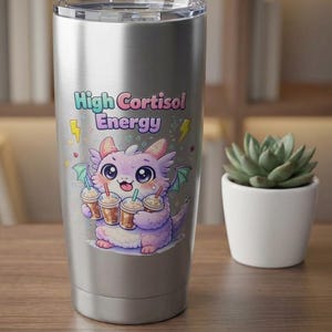 May include: A stainless steel tumbler featuring a cartoon dragon holding coffee cups. The dragon is purple, pink, and green, with the text "High Cortisol Energy" in a colorful font. The tumbler has a silver lid.