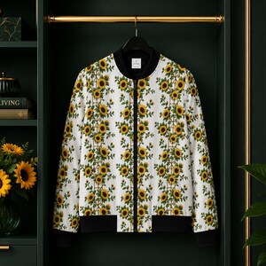 Op de afbeelding: Een wit bomberjack met een herhalend verticaal patroon van gele zonnebloemen met groene bladeren en bruine stelen. Het jack heeft een zwarte geribbelde kraag, zwarte mouwboorden, een zwarte zoom en een centrale zwarte ritssluiting.