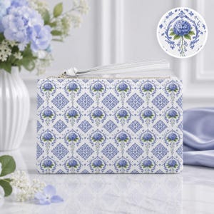 May include: A rectangular white wristlet pouch featuring a repeating pattern of blue hydrangea flowers and intricate blue damask-style scrollwork. The pouch includes a white wrist strap and a gold-toned zipper closure along the top edge.