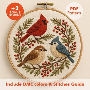 Könnte beinhalten: Gesticktes Stickrahmen-Kunstwerk mit drei Vögeln: einem roten Kardinal, einer Blaumeise und einem braunen Spatz, umgeben von einem Kranz aus grünen Blättern und roten Beeren. Der Text "PDF Pattern" und "+2 Bonus Designs" sind sichtbar. Der Text "Include DMC colors & Stitches Guide" ist ebenfalls sichtbar.