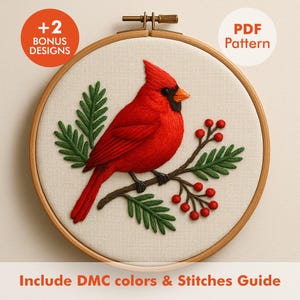 May include: A detailed embroidery hoop featuring a vibrant red cardinal perched on a branch with green leaves and red berries. The design is set against a neutral fabric background, with text indicating bonus designs and a PDF pattern.
