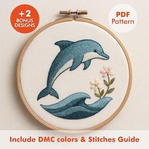 Könnte beinhalten: Gesticktes Delfin-Design in einem Holzreifen. Der Delfin ist blaugrün und weiß und springt über eine blaugrüne Welle. Rosa und weiße Blumen sind ebenfalls gestickt. Text enthält "+2 Bonus Designs", "PDF Pattern" und "Include DMC colors & Stitches Guide".