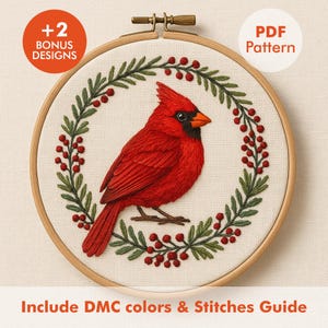 Op de afbeelding: Borduurwerk van een rode kardinaal in een houten hoepel, omringd door een groene en rode krans. De teksten "+2 BONUS DESIGNS" en "PDF Pattern" zijn zichtbaar. De tekst "Include DMC colors & Stitches Guide" staat onderaan.