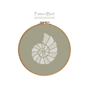 May include: A cross-stitch pattern of a nautilus shell in white and beige colors on a green background. The pattern is framed in a wooden hoop.
