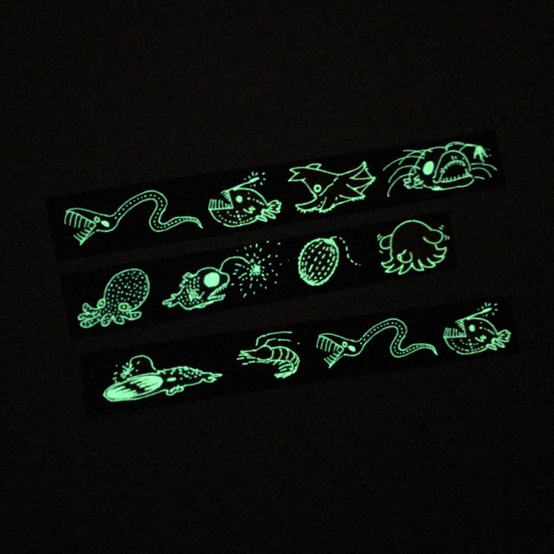 May include: A set of glow-in-the-dark stickers featuring various sea creatures, including a jellyfish, a squid, a fish, and a seahorse. The stickers are black and white and have a whimsical, cartoon-like style.