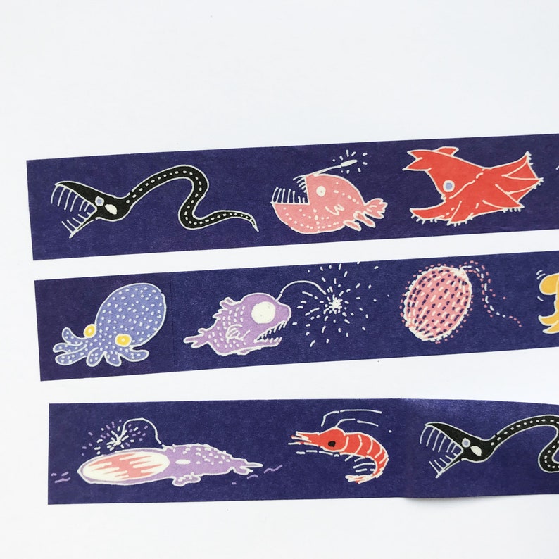 May include: A blue washi tape with a repeating pattern of various deep sea creatures, including a black anglerfish, a red anglerfish, a purple octopus, a purple anglerfish, a red shrimp, and a black eel.