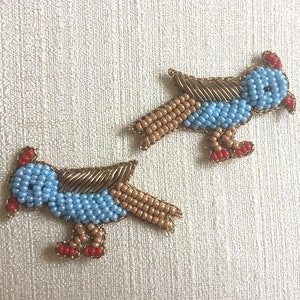 Op de afbeelding: Twee blauwe en bruine kralenvogelapplicaties met rode accenten. De vogels kijken in dezelfde richting en hebben een spanwijdte van ongeveer 7,5 cm.